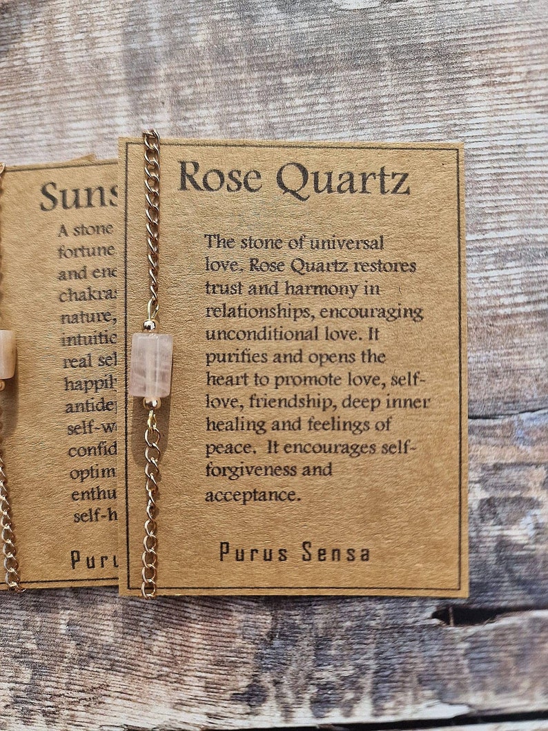 May include: A gold chain necklace with a rose quartz crystal pendant. The card attached to the chain reads "Rose Quartz. The stone of universal love. Rose Quartz restores trust and harmony in relationships, encouraging unconditional love. It purifies and opens the heart to promote love, self-love, friendship, deep inner healing and feelings of peace. It encourages self-forgiveness and acceptance. Purus Sensa."