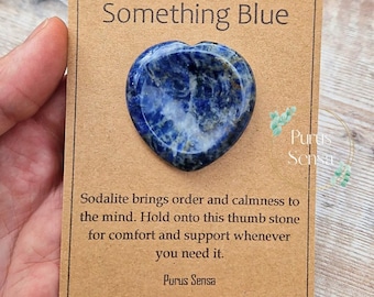 Puede incluir: Una piedra de pulgar de sodalita azul en forma de corazón sobre una tarjeta marrón con el texto "Something Blue" y "La sodalita aporta orden y calma a la mente. Sujeta esta piedra de pulgar para obtener consuelo y apoyo cuando lo necesites. Purus Sensa".