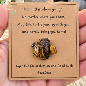 May include: A brown and gold tiger eye stone carved into a turtle shape, mounted on a tan card with the text: No matter where you go, No matter where you roam, May this turtle journey with you, and safely bring you home! Tiger Eye for protection and Good Luck. Purus Sensa.