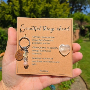 Op de afbeelding: Een sleutelhanger met een houten label met de tekst "You've got this" en een hart. De sleutelhanger heeft een zilveren ring en kralen in geel, helder en roze. Een kaart met "Beautiful things ahead" en beschrijvingen van Citrien, Bergkristal en Zonnesteen is ook zichtbaar.