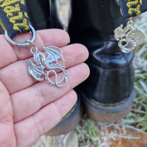 May include: A silver dragon charm attached to a black leather boot with a yellow strap that says "Dr. Martens".