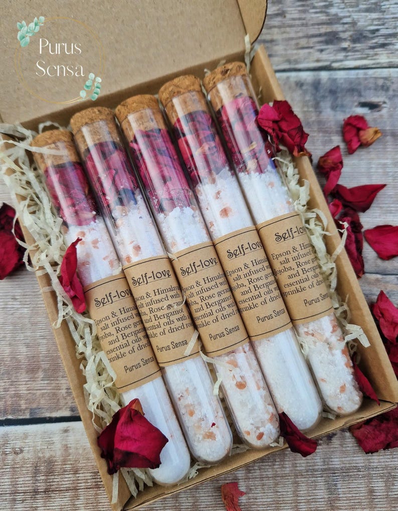 Pu&ograve; includere: Set di sei provette di vetro riempite con sali da bagno bianchi e petali di rosa. Ogni provetta ha un tappo di sughero e un'etichetta che recita "Self-Love" con una descrizione degli ingredienti. Le provette sono disposte in una scatola con carta triturata e petali di rosa.