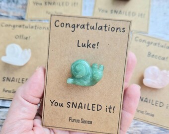 May include: A brown card with the text "Congratulations Luke! You SNAILED it! Purus Sensa" and a green snail figurine.