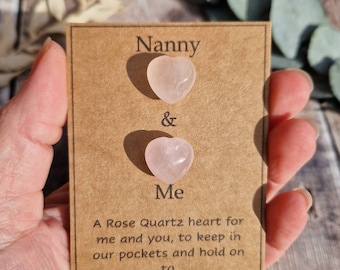 Könnte beinhalten: Zwei herzförmige Steine aus rosa Quarz auf einer braunen Karte mit dem Text "Nanny & Me" und "Ein Herz aus Rosenquarz für mich und dich, zum Aufbewahren in unseren Taschen und zum Festhalten. Purus sensa"