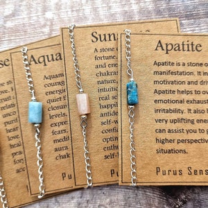 May include: Four silver chain bracelets with different colored gemstone beads and corresponding cards with the names "Rose", "Aqua", "Sun", and "Apatite". Each card describes the stone's properties and meaning.