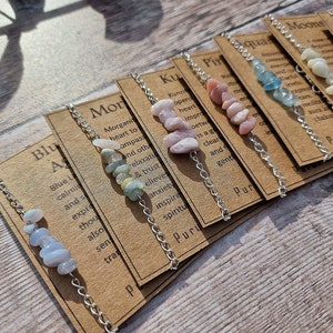 May include: A set of ten bracelets with different colored stones and silver chains. Each bracelet has a card with text describing the stone's properties. The cards include the words "Morganite", "Kunzite", "Pink", "Aquamarine", "Moons", "Larimar", "Blue", "Purus", "Purus", and "Purus".
