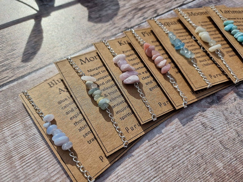 May include: A set of ten bracelets with different colored stones and silver chains. Each bracelet has a card with text describing the stone's properties. The cards include the words "Morganite", "Kunzite", "Pink", "Aquamarine", "Moons", "Larimar", "Blue", "Purus", "Purus", and "Purus".