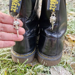 May include: Black leather boots with yellow and black laces and silver skull charms attached to the laces.