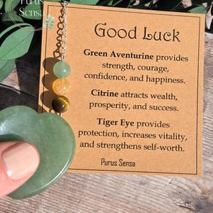 May include: Green Aventurine, Citrine, and Tiger Eye crystal heart charm necklace with a card that reads "Good Luck" and describes the properties of each stone. The card also says "Green Aventurine provides strength, courage, confidence, and happiness. Citrine attracts wealth, prosperity, and success. Tiger Eye provides protection, increases vitality, and strengthens self-worth. Purus Sensa."