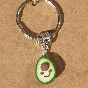 May include: A silver key chain with a green avocado charm. The avocado has a brown pit and a smiling face.