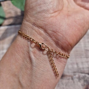 May include: A gold chain bracelet with a lobster clasp closure. The bracelet is shown on a person's wrist.