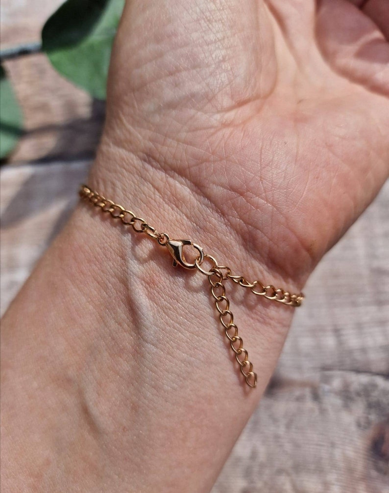 May include: A gold chain bracelet with a lobster clasp closure. The bracelet is shown on a person's wrist.