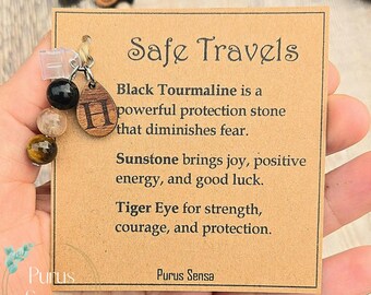 May include: A bracelet with black tourmaline, sunstone, and tiger eye beads. The bracelet is attached to a card that reads "Safe Travels" and describes the properties of each stone. A wooden charm with the letter "H" is also attached.