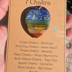 May include: A 7 Chakra stone pendant with a layered design of amethyst, lapis lazuli, sodalite, green aventurine, tiger eye, carnelian, and red jasper. The pendant is on a card with the name of each chakra and the corresponding stone.