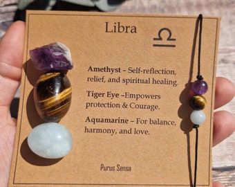 May include: A brown card with the word "Libra" and the astrological symbol for Libra. The card lists the properties of amethyst, tiger eye, and aquamarine crystals. Three crystals are attached to a black string bracelet.