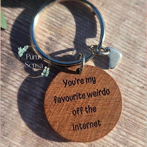 Könnte beinhalten: Ein Holzschlüsselanhänger mit einem silbernen Ring und einem kleinen silbernen Herzanhänger. Der Schlüsselanhänger trägt die Gravur "You're my favourite weirdo off the internet".