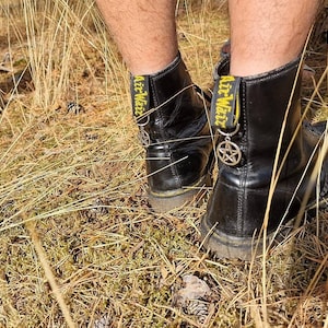 May include: Black leather boots with yellow laces and a pentagram charm. The boots are worn and have a distressed look.