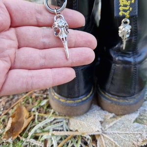 May include: A pair of black leather boots with yellow laces and a silver skull charm attached to one of the laces. The boots are sitting on a bed of fallen leaves covered in frost.