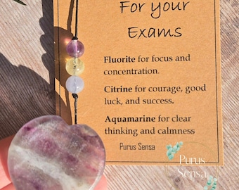 May include: A heart-shaped purple, white, and green fluorite crystal with a card that reads "For your Exams" and lists the properties of fluorite, citrine, and aquamarine crystals. The card also includes the text "Purus Sensa".