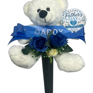 Op de afbeelding: Een witte teddybeer met een zwarte neus en een blauw lint met de tekst "DADDY". De beer is versierd met blauwe rozen en een "Happy Father's Day" bord.