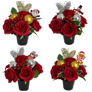 May include: Four black pots containing artificial red rose arrangements. Each features a glittery butterfly, red berries, green leaves, and two spherical ornaments. The arrangements include festive figures: a Santa, a snowman, a penguin, and a gingerbread man.