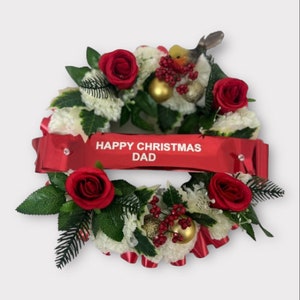 May include: A Christmas wreath with red roses, white flowers, green leaves, and gold ornaments. A red banner across the wreath reads "HAPPY CHRISTMAS DAD". A small bird figurine is perched on top.