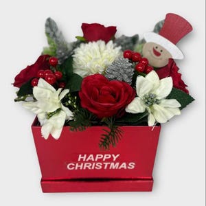 May include: A Christmas floral arrangement in a red box. The arrangement features red roses, white poinsettias, and berries, with a snowman decoration. The box reads "HAPPY CHRISTMAS".