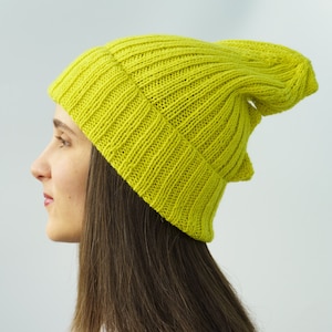 May include: A bright yellow-green knit beanie hat. The hat is made of a ribbed knit fabric and has a slouchy design. The hat is a vibrant color and appears to be made of a soft material. The hat is a stylish accessory.