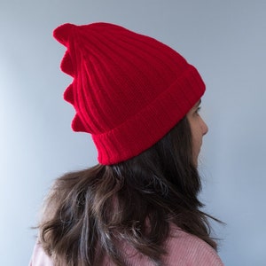 May include: A bright red knit beanie with a unique, pointed design. The hat is ribbed and appears to be made of a soft, warm material. The beanie is a vibrant shade of red, perfect for adding a pop of color to any outfit.