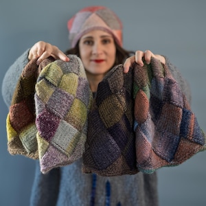 May include: Three knitted hats with a patchwork design are held up. The hats feature a variety of colours, including brown, purple, green, and blue. The person is also wearing a matching hat.