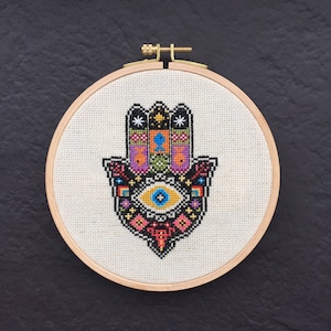 May include: A colourful embroidered hamsa hand with a blue eye in the centre, framed in a wooden hoop.