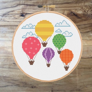 Op de afbeelding: Borduurpatroon met zes kleurrijke luchtballonnen met verschillende patronen, die vliegen in een witte lucht met wolken.