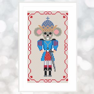 May include: A cross-stitch pattern of a mouse dressed as a nutcracker. The mouse is wearing a blue and red uniform with a gold crown and a sword. The pattern is framed in a red border.