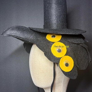 May include: A whimsical black felt hat with a tall cylindrical crown and a wide brim, adorned with yellow circular accents and googly eyes. The hat is designed to resemble a bird or creature, perfect for costume play.