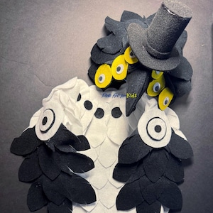 May include: A handmade owl costume made of felt. The costume features a black top hat, black and white feathers, and large yellow and white eyes. The text "Plate Art for Kids" is visible.