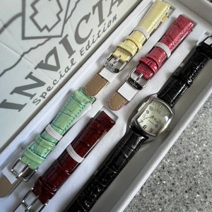 Puede incluir: Un juego de cuatro correas de reloj Invicta edici&oacute;n especial en una caja blanca. Las correas son negras, rojas, verdes y amarillas. La caja tiene el logotipo de Invicta y las palabras "Edici&oacute;n especial".