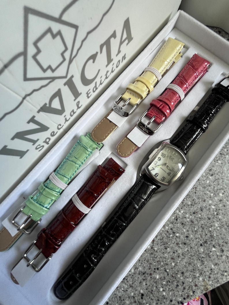 Puede incluir: Un juego de cuatro correas de reloj Invicta edici&oacute;n especial en una caja blanca. Las correas son negras, rojas, verdes y amarillas. La caja tiene el logotipo de Invicta y las palabras "Edici&oacute;n especial".