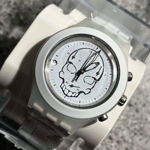 May include: White wristwatch with a white silicone band and a white face. The face features a black skull graphic and the word "Swatch" printed on the face.