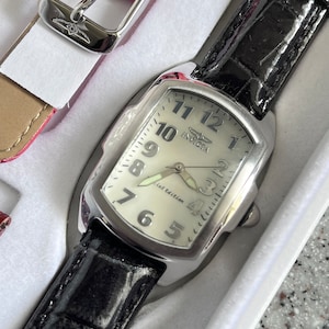 Puede incluir: Un reloj plateado con una correa de cuero negro. La esfera del reloj es blanca con n&uacute;meros negros y las palabras "First Edition" impresas en ella. El reloj tiene una caja plateada y una correa plateada.