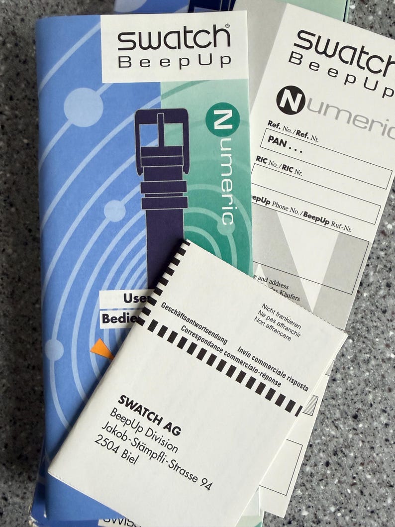 May include: A stack of Swatch BeepUp watch instruction manuals and paperwork. The main booklet is blue with a watch strap illustration. Additional paperwork includes the "Numeric" logo and address information for SWATCH AG.