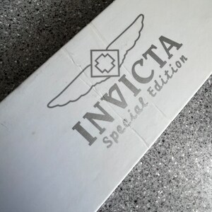 Puede incluir: Caja blanca con un logotipo Invicta plateado y las palabras "edici&oacute;n especial" impresas en ella.