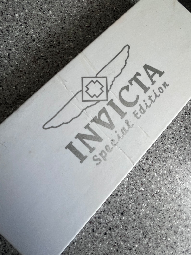 Puede incluir: Caja blanca con un logotipo Invicta plateado y las palabras "edici&oacute;n especial" impresas en ella.