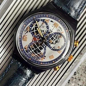 May include: A blue and silver Swatch watch with a chronograph and a world map design on the face. The watch has a blue leather strap.