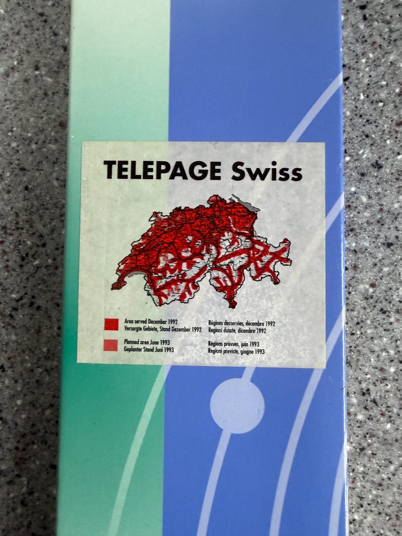 May include: A rectangular graphic with the text "TELEPAGE Swiss" and a red map of Switzerland. The graphic includes text in English, French, and Italian, detailing area served and planned area with dates.