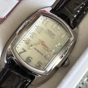 Puede incluir: Un reloj Invicta plateado con una esfera blanca y una correa de cuero negra. La esfera del reloj tiene marcadores de hora romanos negros y una aguja de segundos plateada. La esfera del reloj tambi&eacute;n tiene el texto "Invicta" y "Special Edition".