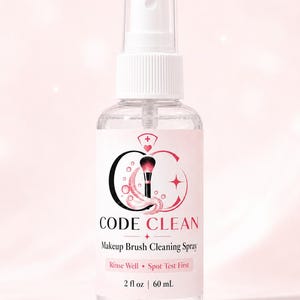 May include: A clear plastic spray bottle containing makeup brush cleaning solution. The label features the text CODE CLEAN, Makeup Brush Cleaning Spray, Rinse Well, Spot Test First, and 2 fl oz | 60 mL, with a graphic of a makeup brush.