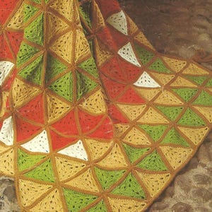 Pode incluir: Uma manta de crochê colorida com um padrão geométrico de triângulos em tons de vermelho, verde, amarelo e branco. A manta tem uma borda marrom e borlas nos cantos. O texto "No. 6506 (Página 22)" é visível.