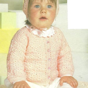 Puede incluir: Un bebé con una chaqueta, gorro y pantalón blancos de ganchillo rosa claro. La chaqueta tiene botones rosas y un cuello de encaje blanco. El texto "Crochet Jacket, Cap and Afghan" es visible.