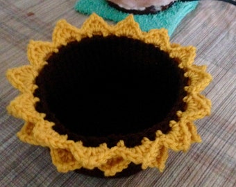 May include: A crocheted sunflower-shaped bowl with a brown center and yellow petals.