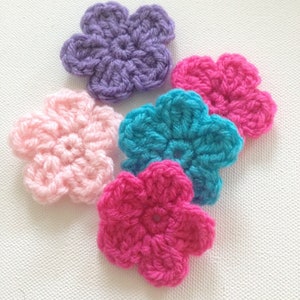 May include: Five crocheted flowers in different colours: purple, pink, teal, and hot pink. The flowers are all the same size and shape, with five petals and a small centre hole.